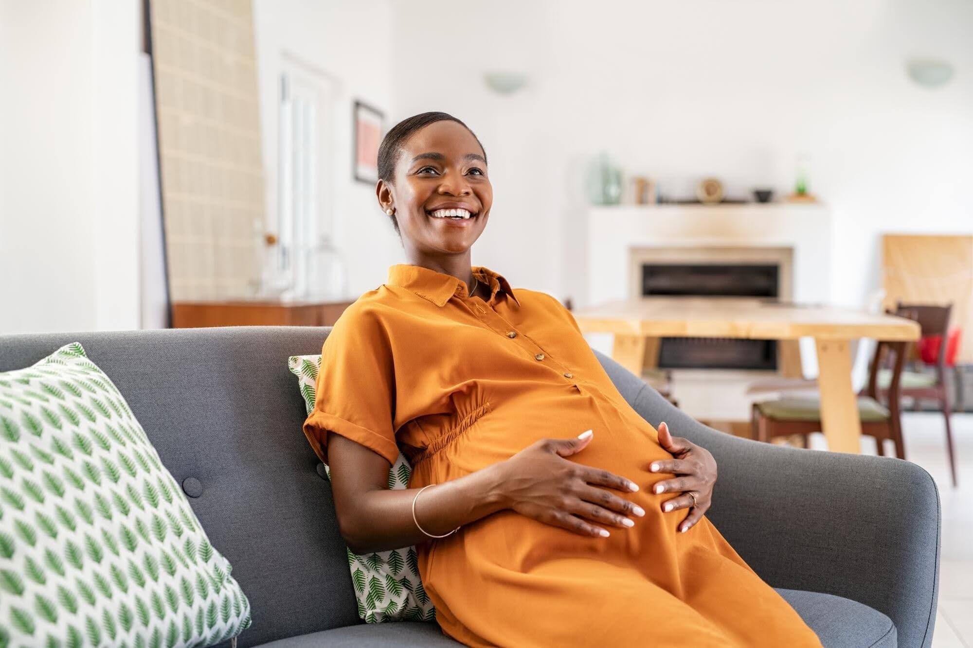 Pregnant woman smiling and holding her stomach sitting on a couch